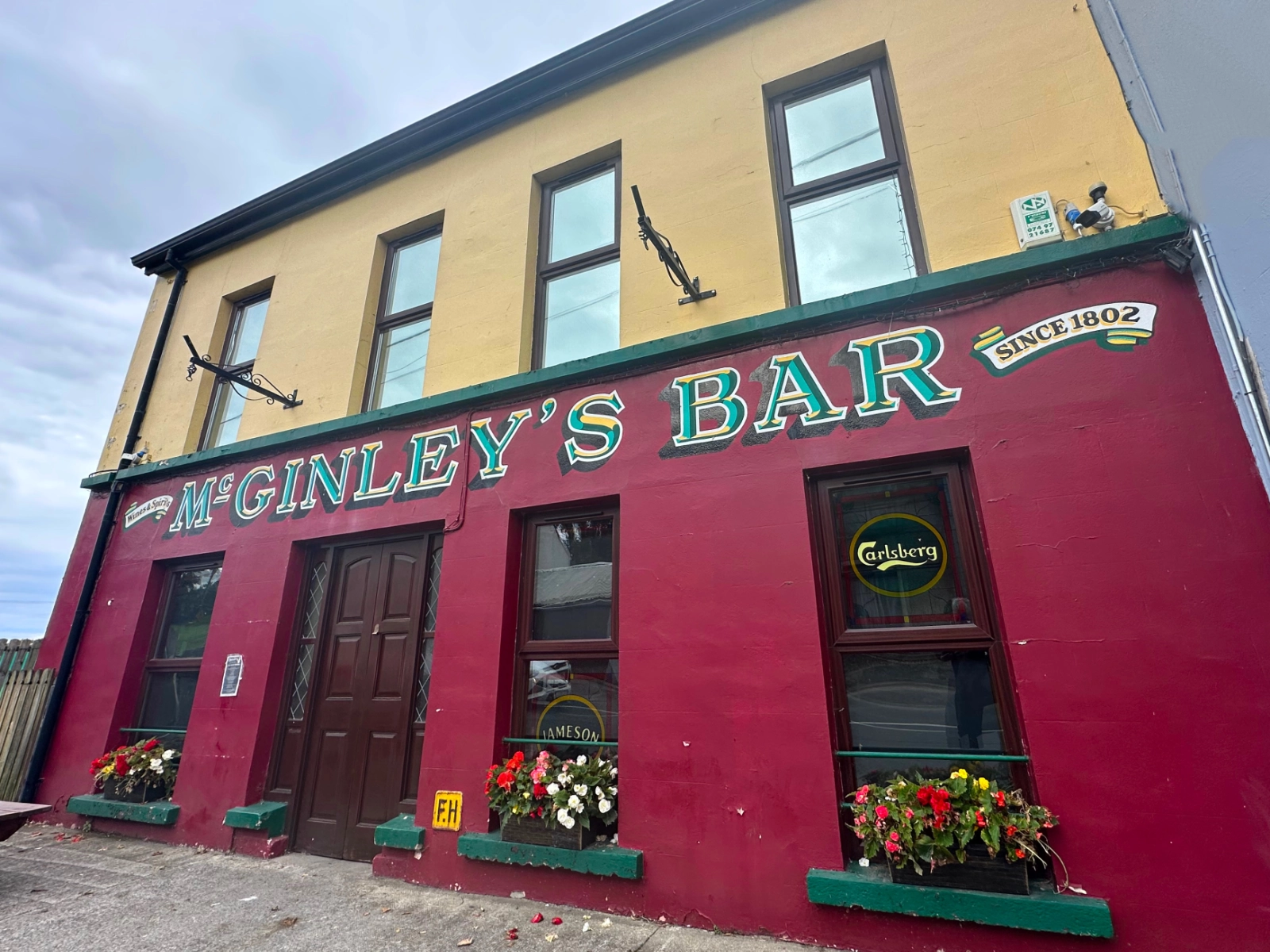 Exterior view of McGinley's Bar featuring a red facade with hanging flower baskets classic signage and a clear sky reflecting its historic charm and inviting ambiance