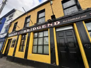 An exterior photo of the Bridgend Bar in Ballyshannon Ireland. It's yellow and black facade shows the distinctive text and decoration of a classic Irish pub.